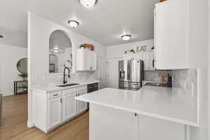 Kitchen featuring a peninsula, appliances with stainless steel finishes, white cabinets, light wood finished floors, and arched walkways