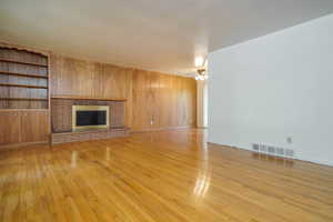 Unfurnished living room featuring light wood-style floors, a fireplace, and wood walls