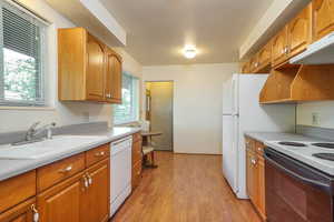 Kitchen featuring light wood-type flooring, light countertops, white appliances, brown cabinets, and under cabinet range hood