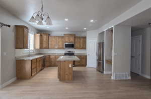 Kitchen featuring a center island, brown cabinets, hanging light fixtures, light wood finished floors, and recessed lighting