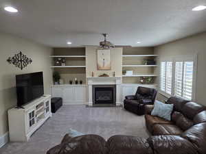 Carpeted living room featuring a fireplace with flush hearth, recessed lighting, and ceiling fan
