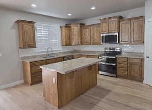 Kitchen with appliances with stainless steel finishes, brown cabinetry, recessed lighting, a center island, and light wood-type flooring