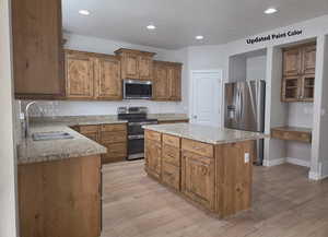 Kitchen with stainless steel appliances, a center island, brown cabinetry, light wood-type flooring, and recessed lighting