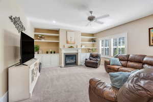 Living area with built in shelves, a fireplace with flush hearth, a ceiling fan, and a textured ceiling