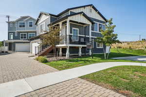View of front of house with board and batten siding, decorative driveway, a front lawn, covered porch, and stairway