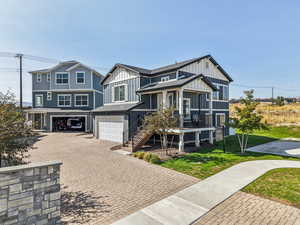 View of front of property featuring board and batten siding, decorative driveway, a garage, stairway, and covered porch