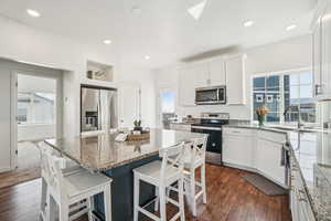 Kitchen featuring a kitchen breakfast bar, light stone countertops, white cabinets, stainless steel appliances, and healthy amount of natural light