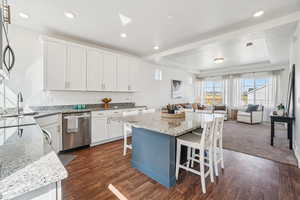 Kitchen with white cabinets, a tray ceiling, light stone countertops, a center island, and appliances with stainless steel finishes