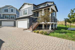 View of front of house with an attached garage, decorative driveway, board and batten siding, stairs, and a front yard