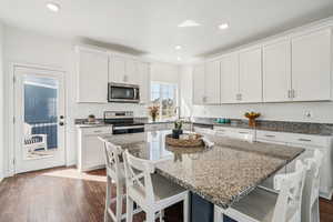Kitchen featuring a breakfast bar area, appliances with stainless steel finishes, dark wood-style flooring, white cabinetry, and dark stone counters