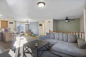 Living room with a chandelier, dark wood-style floors, ornamental molding, and ceiling fan
