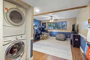 Laundry area with wood finished floors, stacked washer and clothes dryer, and ceiling fan
