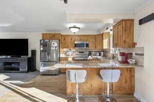 Kitchen featuring stainless steel appliances, light stone counters, backsplash, a kitchen breakfast bar, and a peninsula