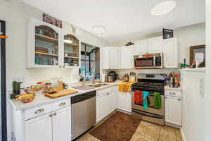 Kitchen featuring stainless steel appliances, white cabinets, glass insert cabinets, and light tile patterned floors