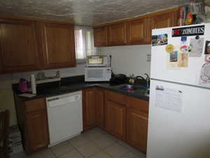 Kitchen featuring white appliances, brown cabinets, dark countertops, and light tile patterned floors