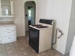 Kitchen with white range with gas cooktop, arched walkways, light tile patterned floors, white cabinets, and light countertops