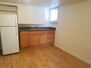 Kitchen with freestanding refrigerator, open shelves, light wood-style floors, and brown cabinetry