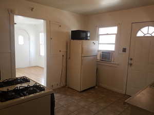 Kitchen featuring white appliances, arched walkways, light tile patterned floors, and cooling unit