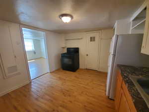 Kitchen featuring black gas range oven, light wood-style flooring, freestanding refrigerator, open shelves, and dark stone counters