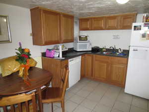 Kitchen with white appliances, dark countertops, light tile patterned floors, and brown cabinetry