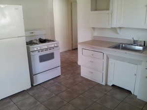 Kitchen with white appliances, white cabinetry, light countertops, and dark tile patterned floors