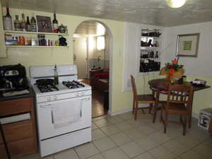 Kitchen with white range with gas cooktop, arched walkways, light tile patterned floors, open shelves, and a textured ceiling