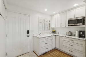 Kitchen with white cabinets, light wood-style floors, stainless steel microwave, light stone countertops, and recessed lighting