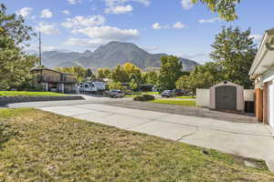 View of green lawn featuring a mountain view, a shed, and driveway