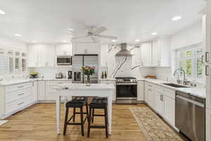 Kitchen with plenty of natural light, appliances with stainless steel finishes, white cabinets, light stone counters, and recessed lighting