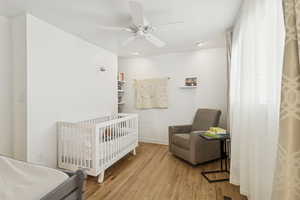 Bedroom featuring a crib, light wood-style floors, and a ceiling fan