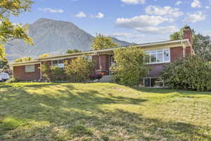 Single story home with a front lawn, brick siding, a mountain view, and a chimney