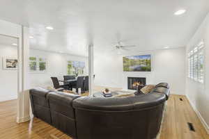 Living area with light wood finished floors, a glass covered fireplace, recessed lighting, and a ceiling fan