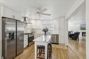 Kitchen with stainless steel appliances, white cabinets, light wood-type flooring, a glass covered fireplace, and recessed lighting