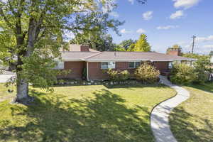 Ranch-style house with brick siding, a chimney, a front yard, and roof with shingles