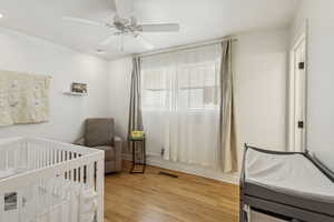 Bedroom with light wood-type flooring, a ceiling fan, and a nursery area