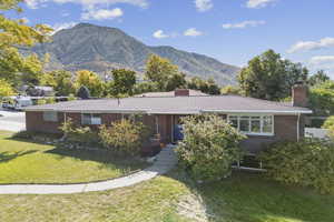 Ranch-style home featuring a chimney, a front lawn, brick siding, and a mountain view