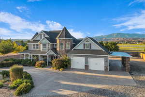View of front facade featuring stone siding, covered porch, driveway, a garage, and a mountain view