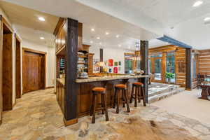 Indoor bar featuring recessed lighting, light stone finish flooring, open shelves, and light stone countertops