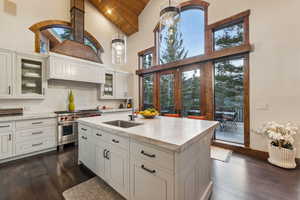 Kitchen with pendant lighting, high vaulted ceiling, glass insert cabinets, backsplash, and dark wood-type flooring
