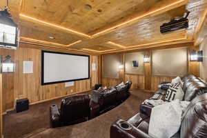 Cinema room with a wood ceiling with exposed beams, wood walls, and carpet flooring