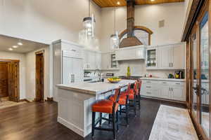 Kitchen with backsplash, hanging light fixtures, dark wood-type flooring, a high ceiling, and a kitchen bar
