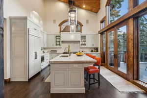 Kitchen featuring glass insert cabinets, high vaulted ceiling, dark wood-type flooring, tasteful backsplash, and a breakfast bar area