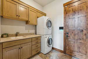 Washroom featuring stacked washer / dryer, stone tile flooring, and cabinet space