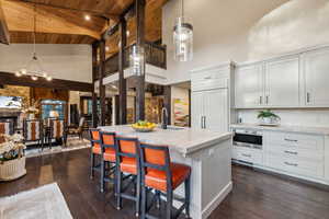 Kitchen with a breakfast bar area, dark wood finished floors, light stone countertops, an island with sink, and a high ceiling