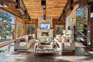 Living area with wooden walls, high vaulted ceiling, a wooden ceiling with exposed beams, a stone fireplace, and wood finished floors