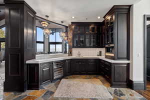 Indoor wet bar featuring healthy amount of natural light, a chandelier, tasteful backsplash, beverage cooler, and recessed lighting