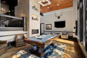 Game room featuring hardwood / wood-style floors, billiards table, a high ceiling, a fireplace, and a chandelier