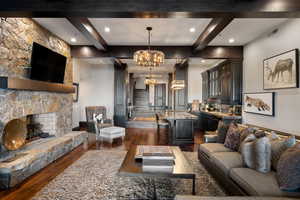 Living room featuring dark wood-style floors, a stone fireplace, beam ceiling, recessed lighting, and a chandelier