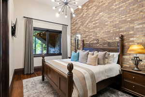 Bedroom featuring dark wood finished floors, a chandelier, and brick wall