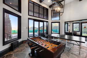 Recreation room featuring stone tile flooring, a chandelier, beam ceiling, a high ceiling, and a mountain view
